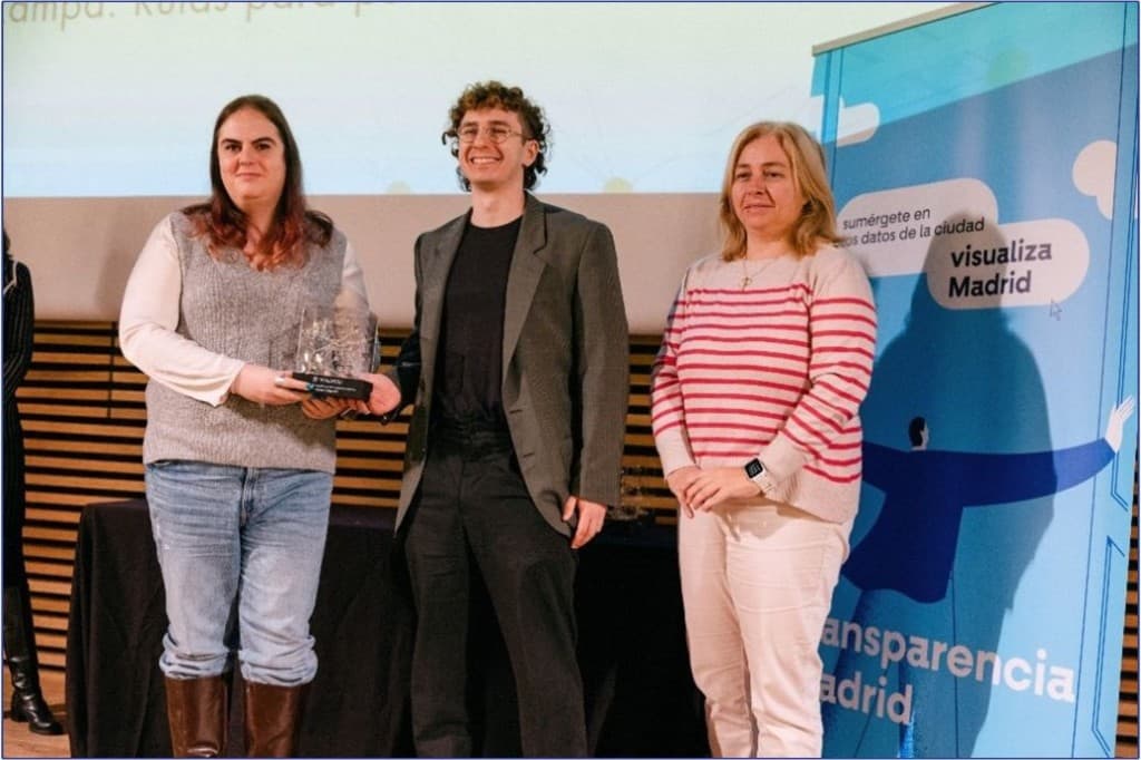 Equipo de la agrupación Rampa con representación municipal en el acto de entrega del premio; trofeo de cristal y cartel de la campaña Visualiza Madrid al fondo.